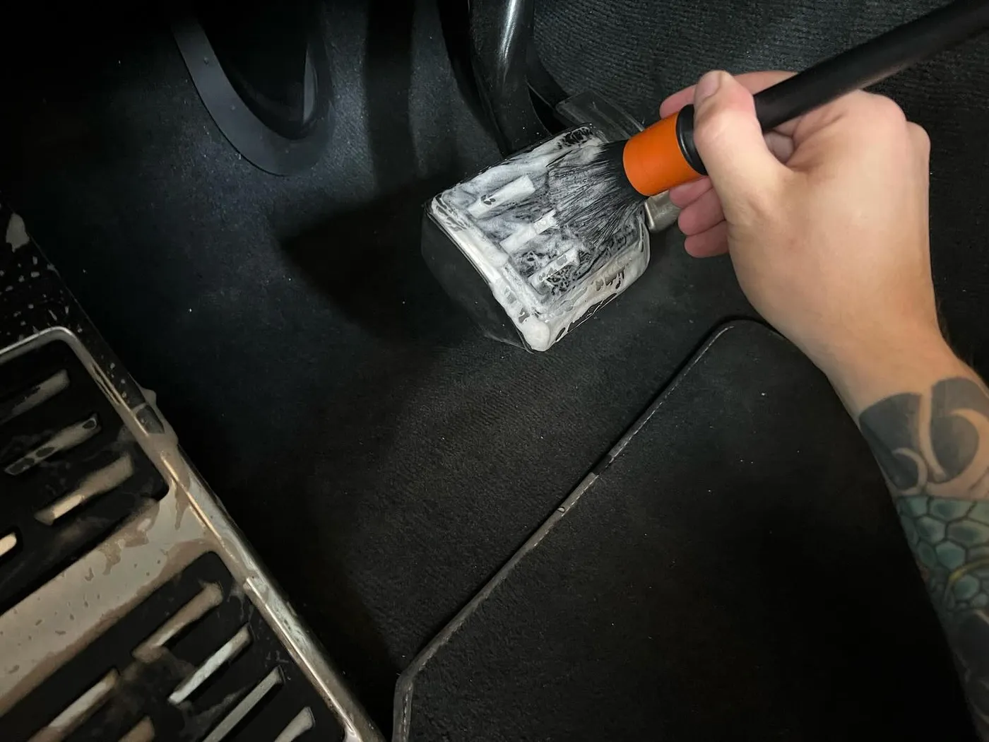 Detailreinigung mit dem Pinsel an Pedalen und Fußraum eines Kundenfahrzeugs