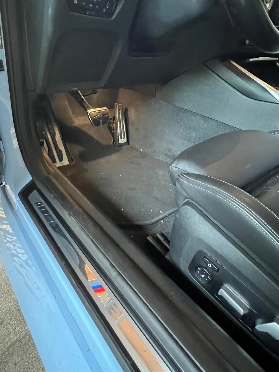 Fahrerfußraum eines BMW M2 vor der Reinigung mit Staub auf der Matte